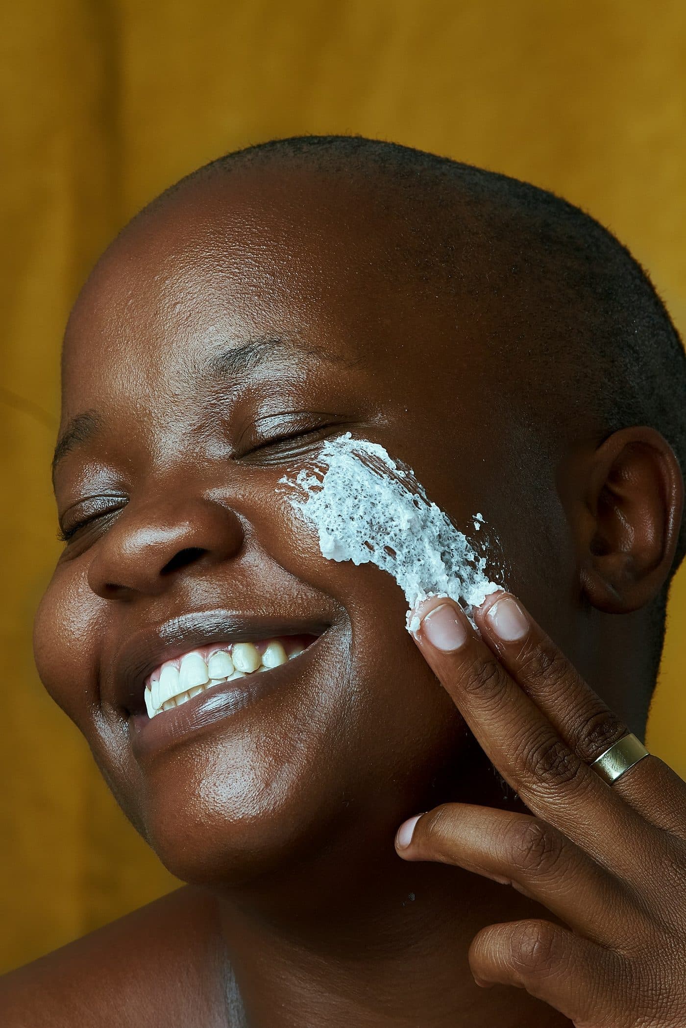 Woman laughing as she smooths a face mask onto her cheek